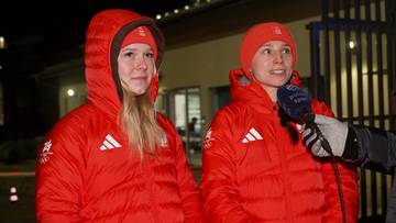 Dwie kobiety w czerwonych kurtkach i czapkach z logo sportowym są przepytywane przez dziennikarza z mikrofonem.