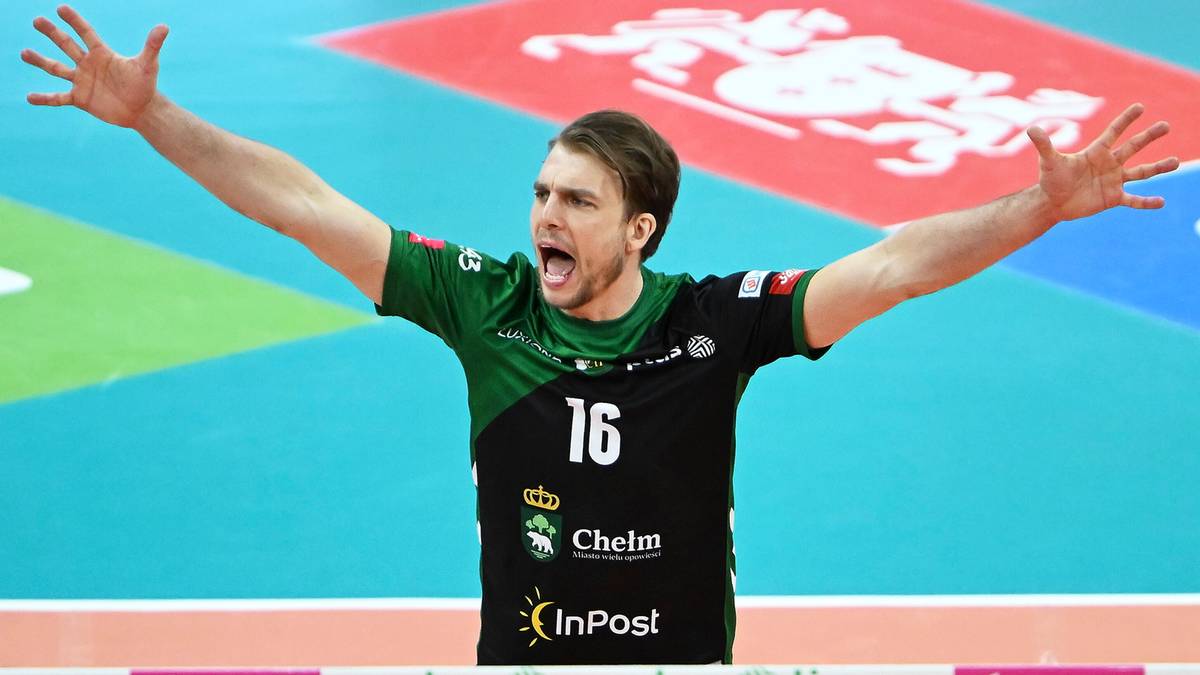 Siatkarz w czarno-zielonej koszulce z numerem 16 rozkłada ręce w geście radości lub krzyku na tle boiska siatkarskiego.