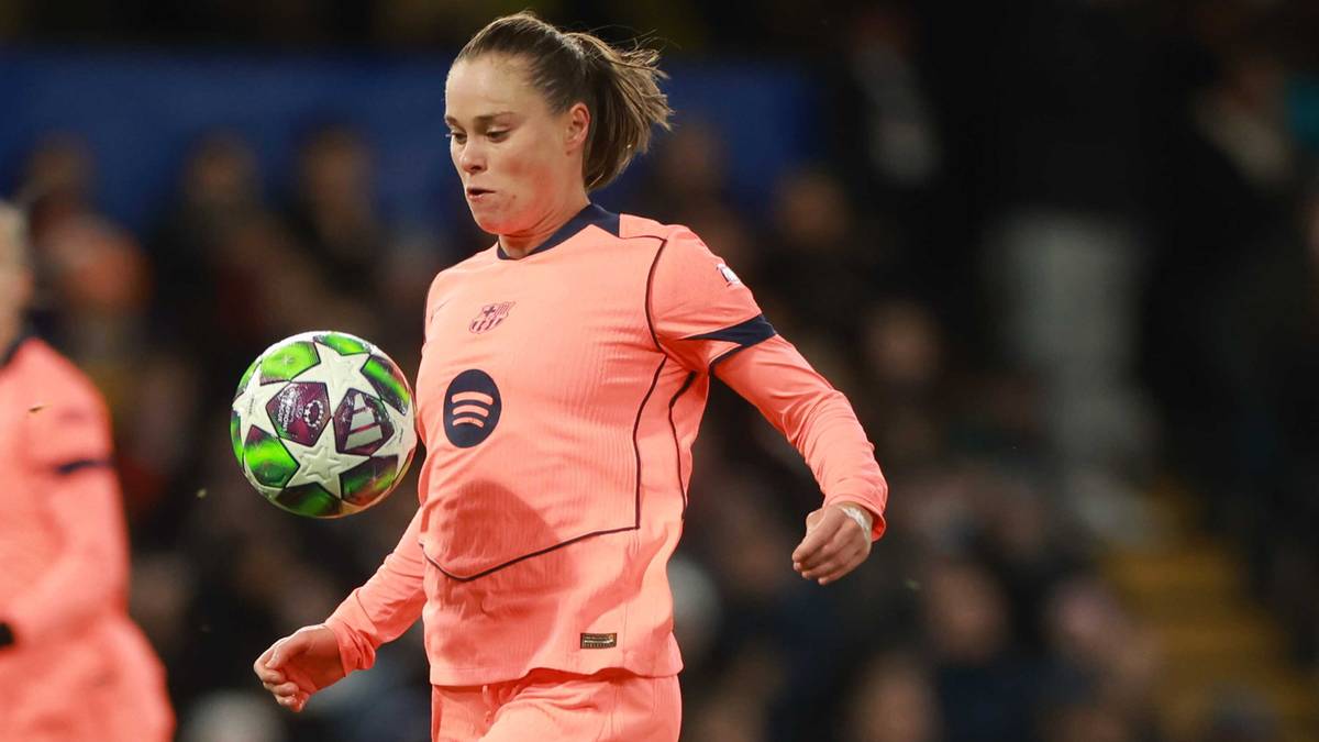 Piłkarka w pomarańczowym stroju prowadzi piłkę, a zawodniczka w niebieskim próbuje ją odebrać