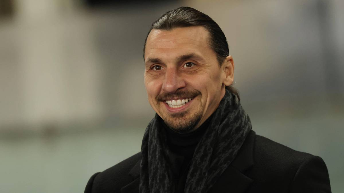 Uśmiechnięty Zlatan Ibrahimović w czarnym płaszczu i szaliku.