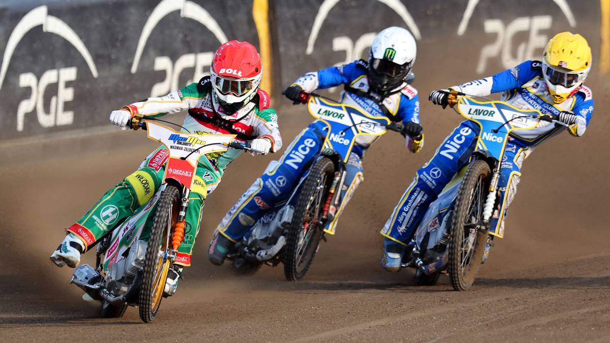 Trzech zawodników na motocyklach żużlowych podczas wyścigu, zmagających się o pozycję na torze.