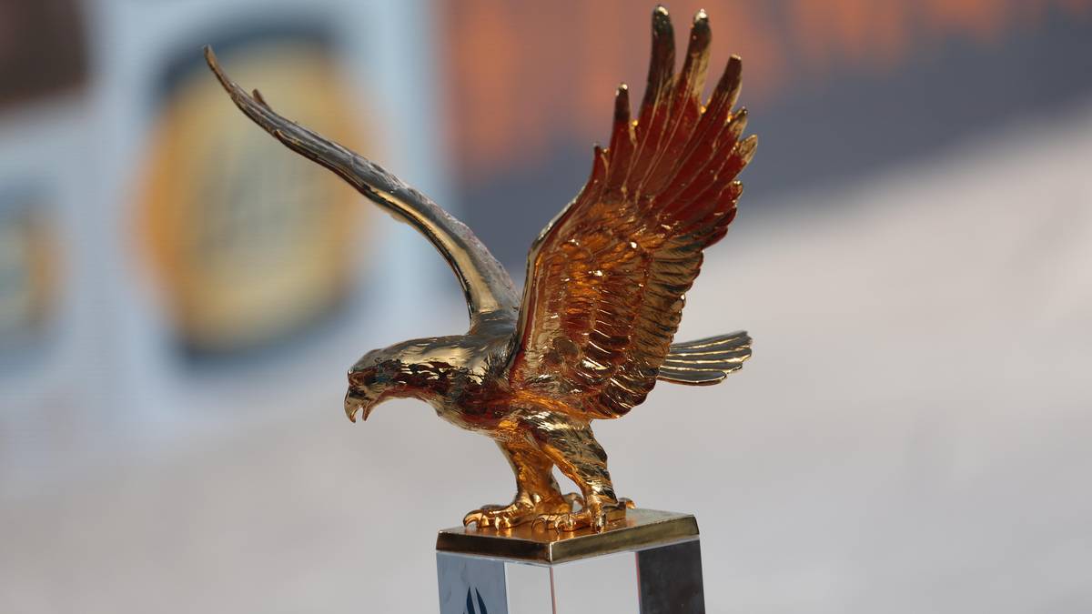 Złota statuetka orła na przezroczystej podstawie z logo.