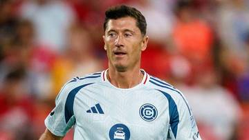 Robert Lewandowski w jasnej koszulce piłkarskiej na tle trybun.