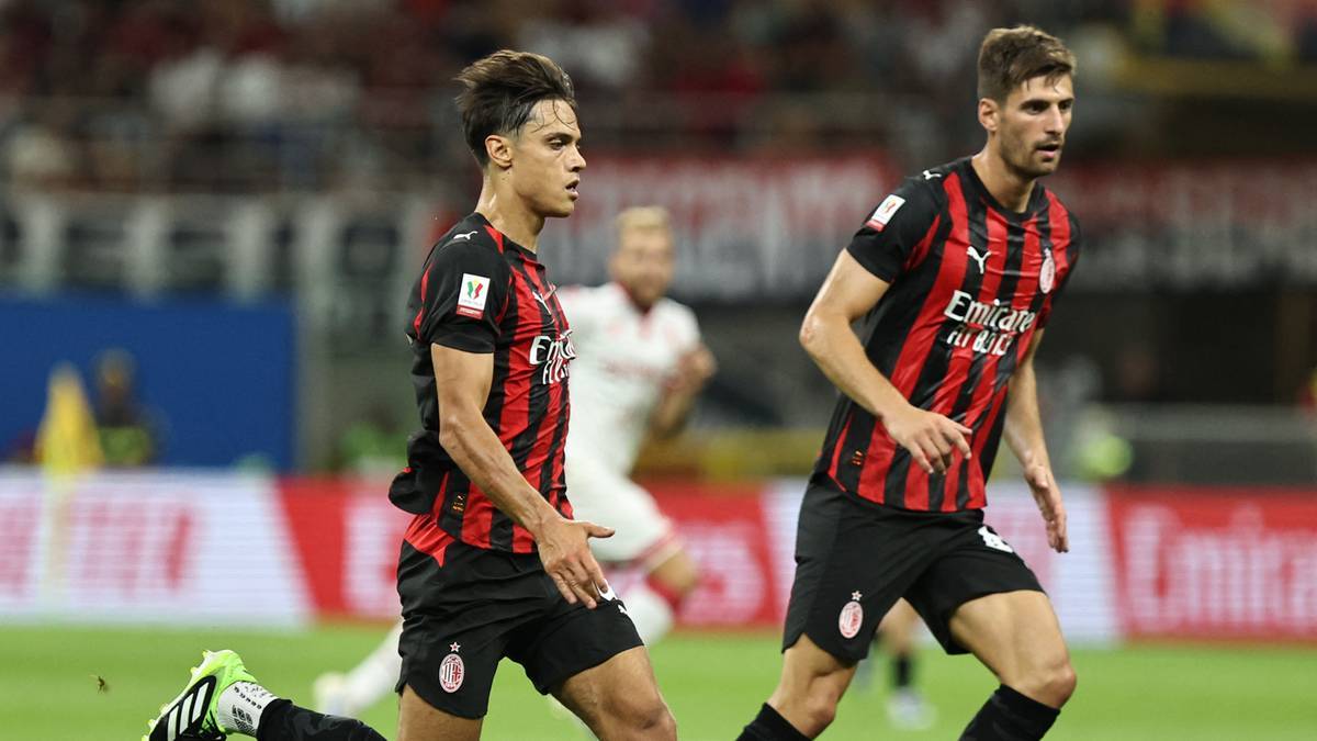 Dwóch piłkarzy w czarno-czerwonych strojach AC Milan biegnie po boisku.