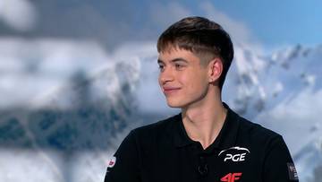 Młody mężczyzna w czarnej koszulce z logo PGE i 4F, z kr&oacute;tkimi, ciemnymi włosami, uśmiecha się.