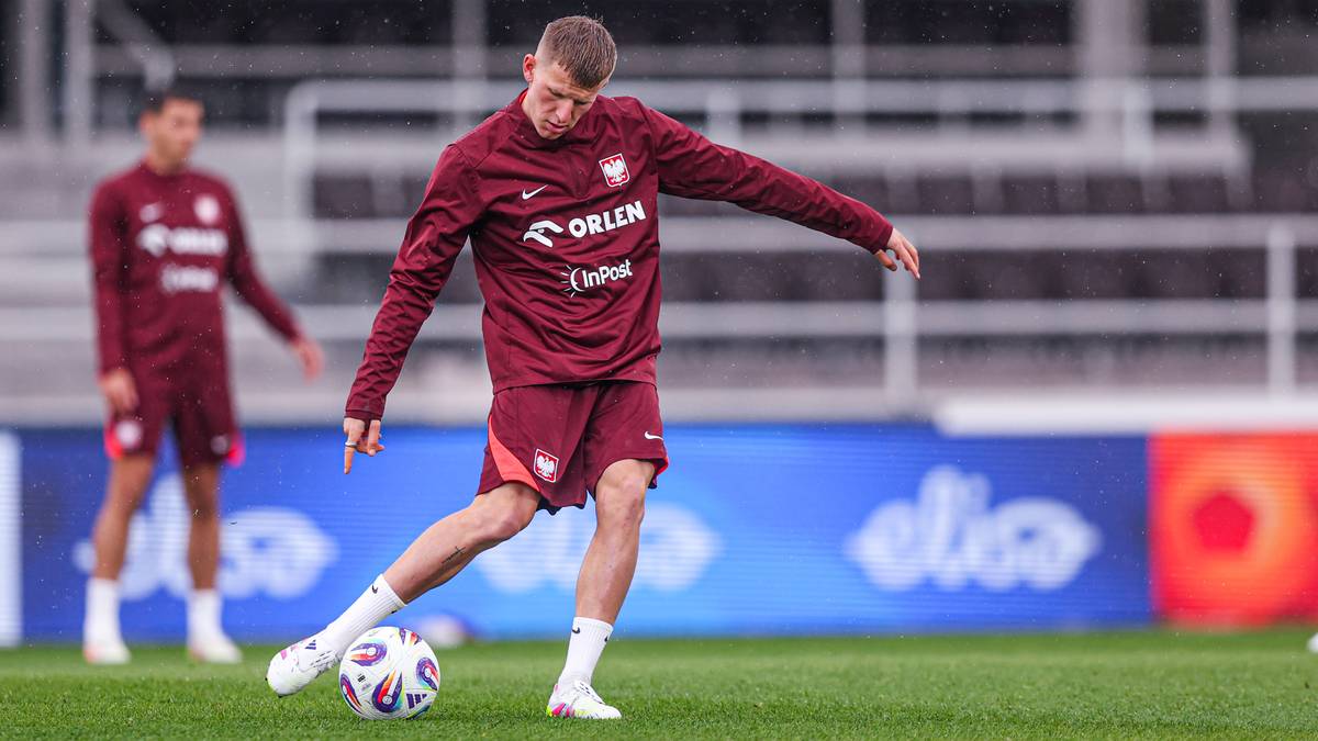 Piłkarz w bordowej koszulce treningowej wykonuje kopnięcie piłki.