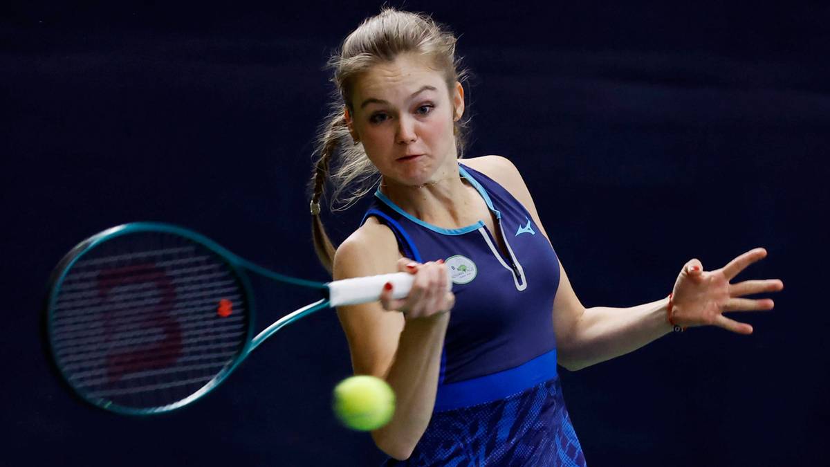 Kobieta w sportowym stroju uderza piłkę tenisową rakietą, skupiona na grze.