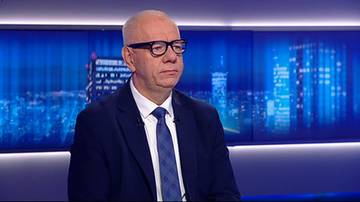 Jacek Sasin w garniturze i okularach w studiu telewizyjnym na tle niebieskich ekran&oacute;w