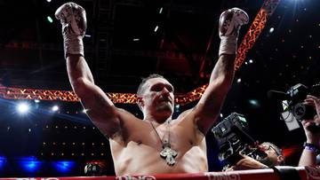 Bokser Oleksandr Usyk z podniesionymi rękami w geście zwycięstwa na ringu.