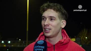 Marek Kania, młody mężczyzna o jasnej karnacji i kręconych włosach, ubrany w czerwoną bluzę z kapturem, udziela wywiadu.