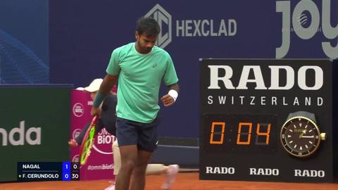 Tenisista Sumit Nagal w zielonej koszulce i granatowych spodenkach na korcie tenisowym, patrzący w bok, z tablicą wynik&oacute;w RADO w tle pokazującą 0:04.