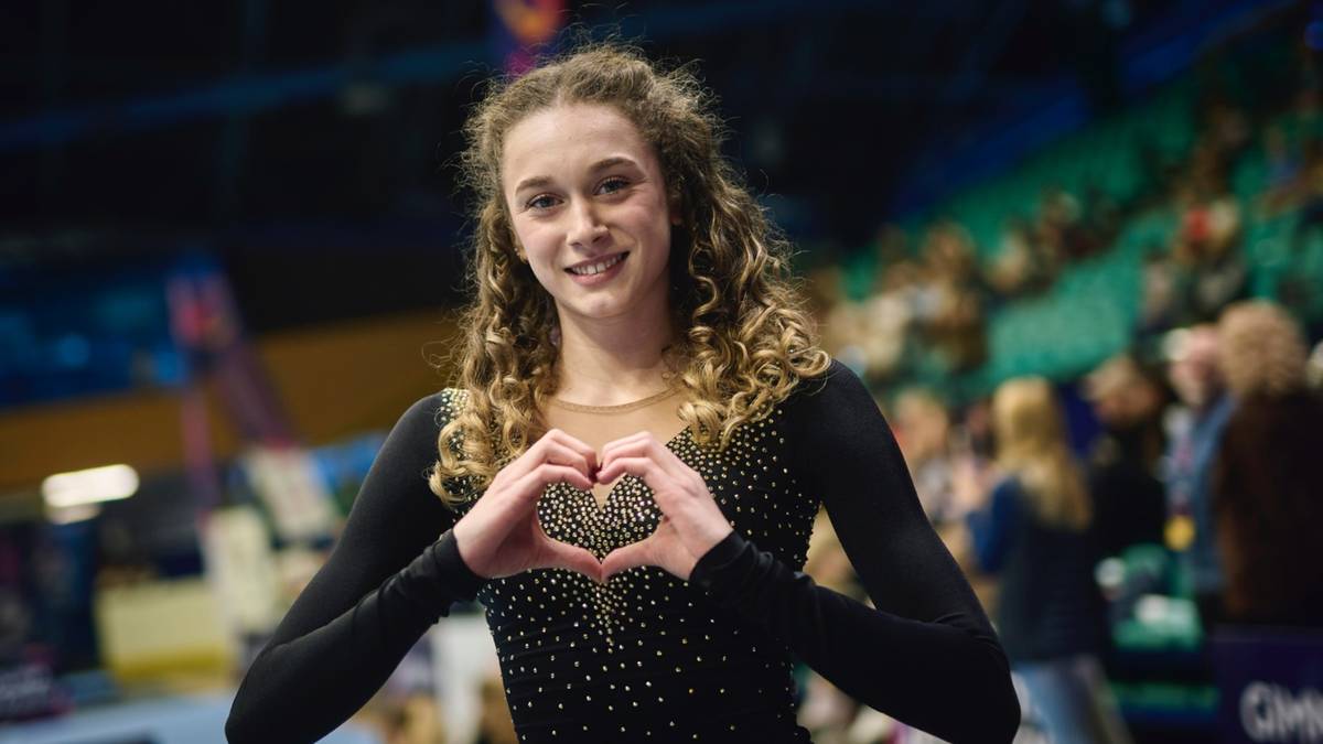 Młoda gimnastyczka artystyczna w czarnym stroju z sercem uformowanym z dłoni.