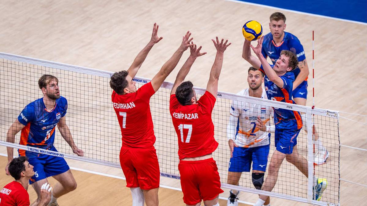 Siatkarze w czerwonych strojach próbują zablokować atak gracza w niebieskim stroju, który wykonuje wyskok do zagrania piłki.