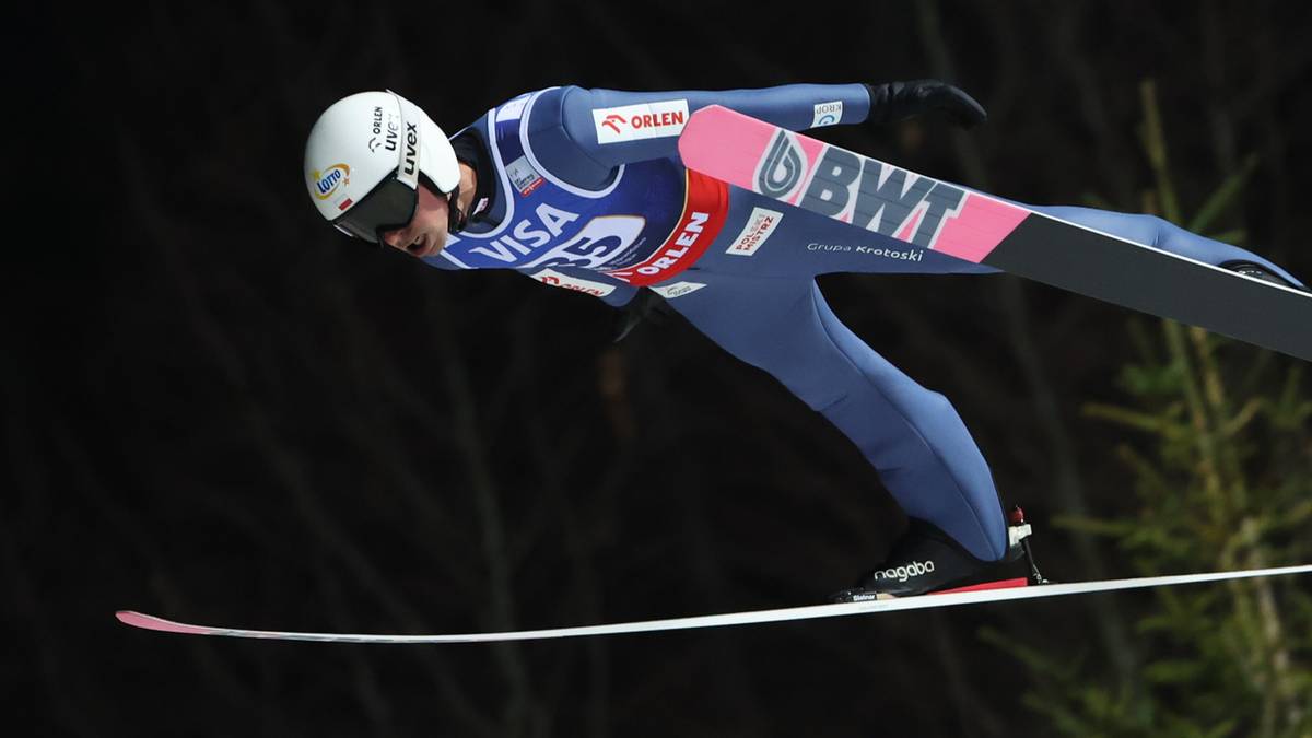 Skoczek narciarski w kombinezonie i kasku wykonuje skok, lecąc na nartach.