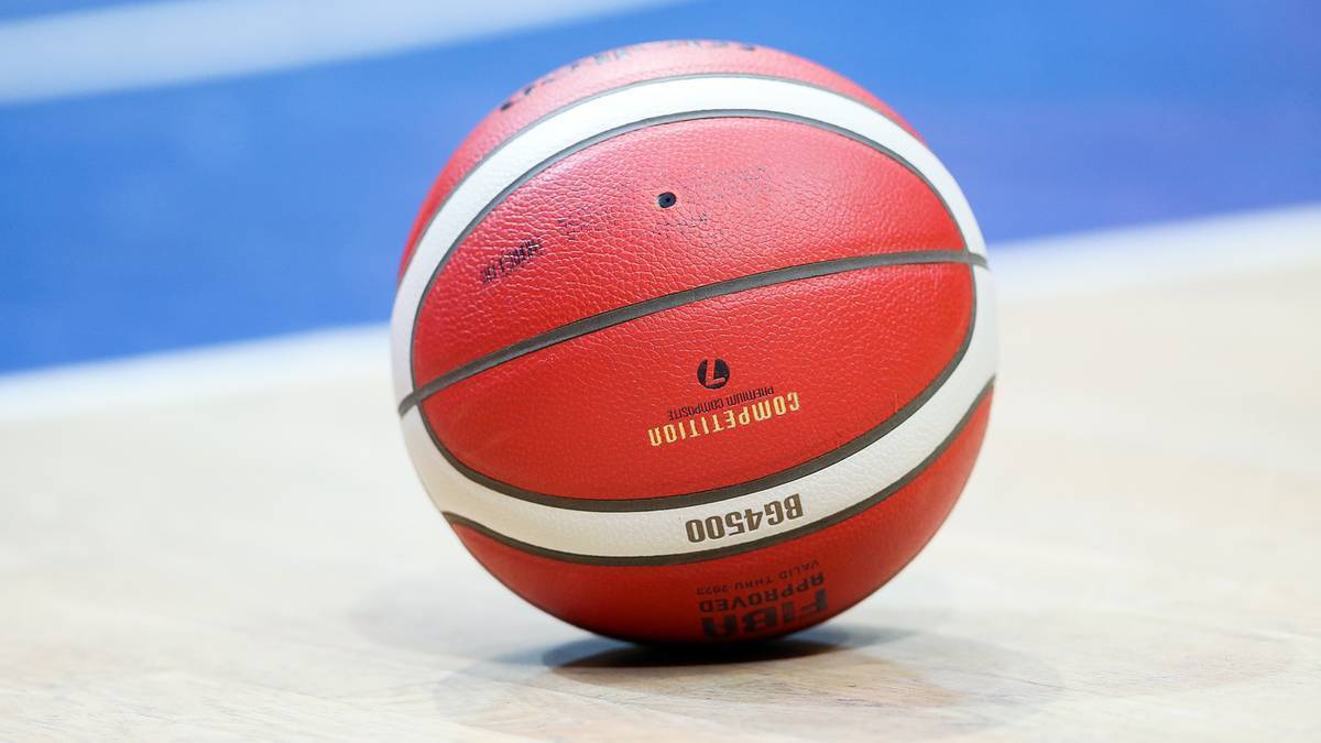 Czerwona piłka do koszyk&oacute;wki z białymi pasami, na parkiecie hali sportowej.