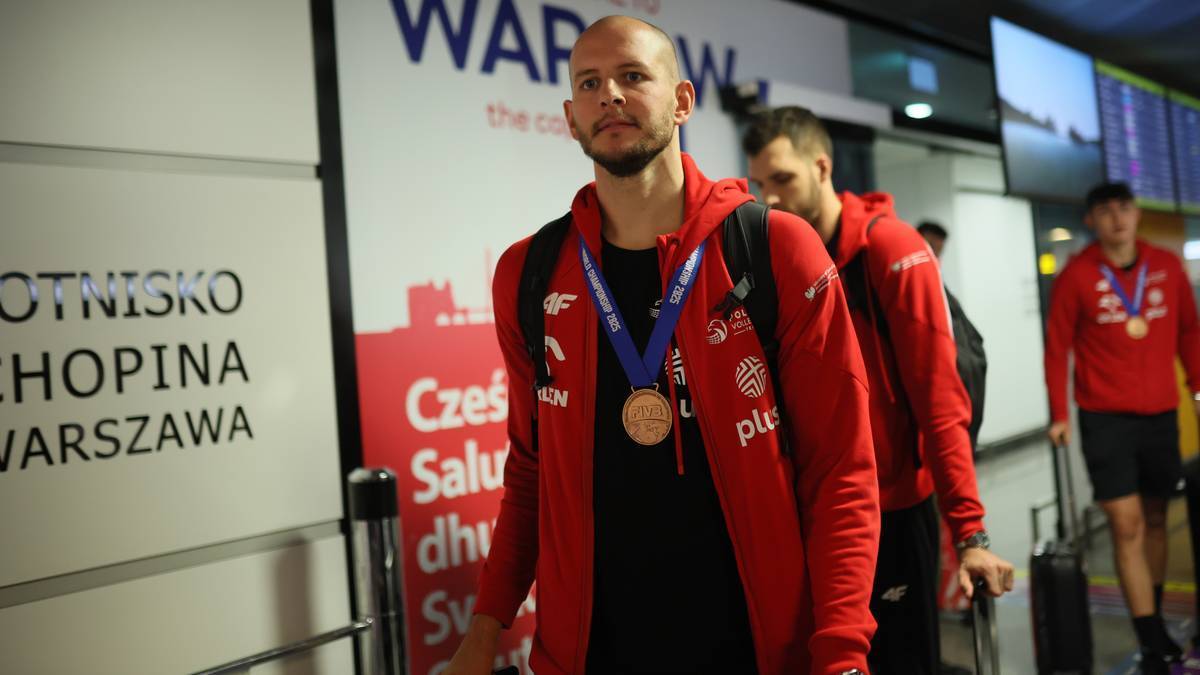 Siatkarz Bartosz Kurek w czerwonej bluzie z medalem na szyi idzie przez lotnisko.