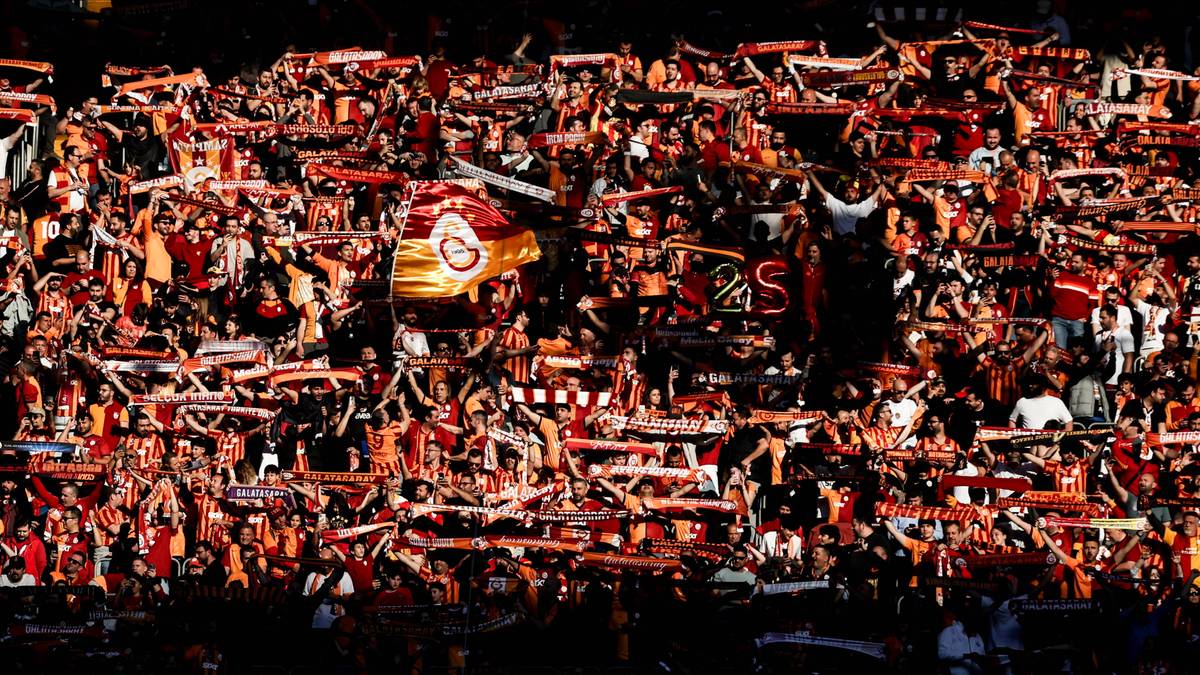 Tłum kibic&oacute;w na stadionie w barwach klubowych, unoszących szale i flagi.