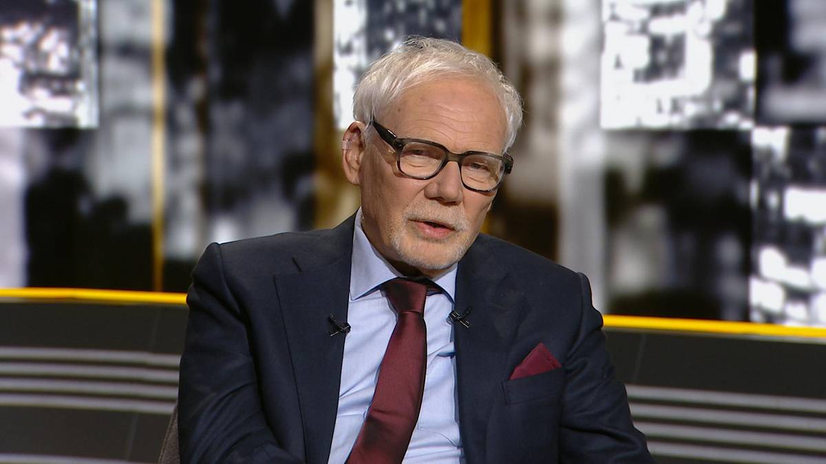 Profesor prawa w okularach, ubrany w garnitur i krawat, siedzi i m&oacute;wi do kamery.