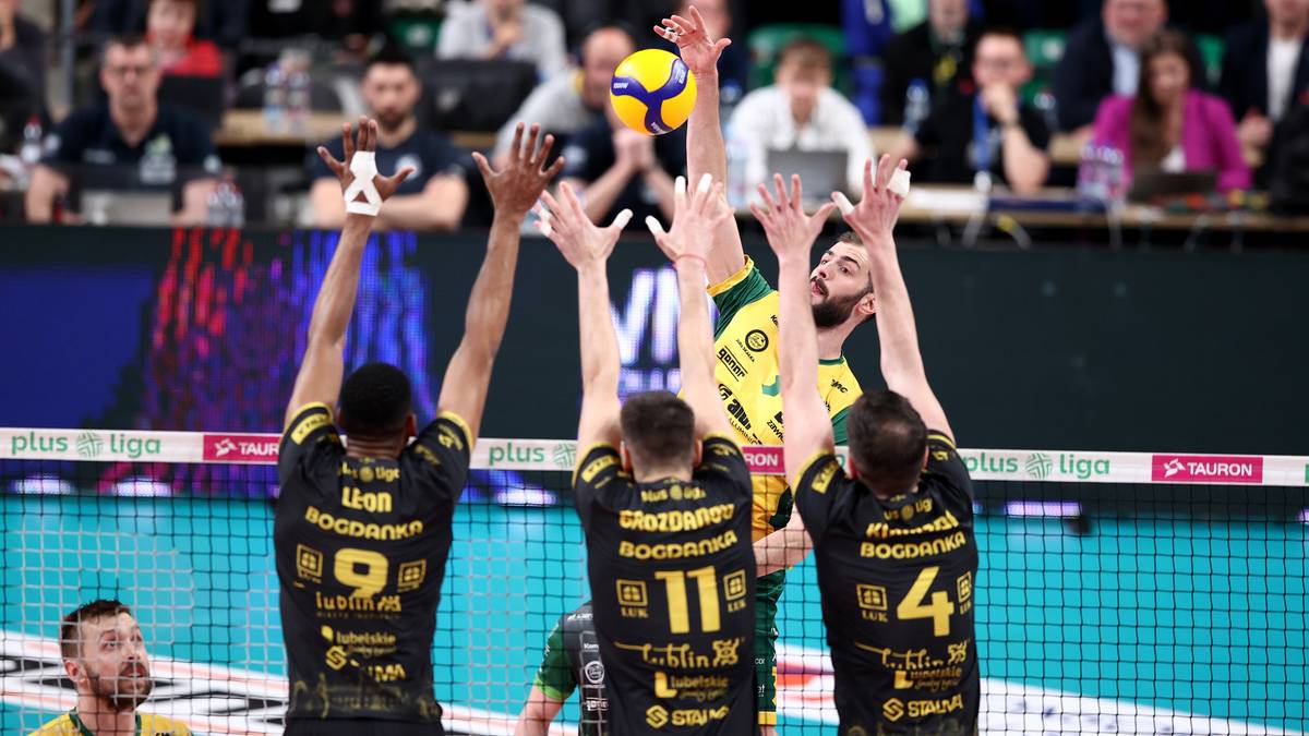 Siatkarz w czarnej koszulce z numerem 9 na plecach unosi ręce w geście radości po zdobyciu punktu. Dwóch innych siatkarzy z tej samej drużyny, w podobnych strojach, również cieszy się ze zwycięstwa, podnosząc ręce. Na pierwszym planie widać fragment twarzy jednego z zawodników, a w tle innych graczy i widzów.