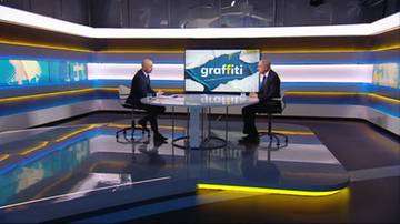 Dw&oacute;ch mężczyzn w garniturach siedzi przy stole w studiu telewizyjnym, na ekranie w tle napis "graffiti".