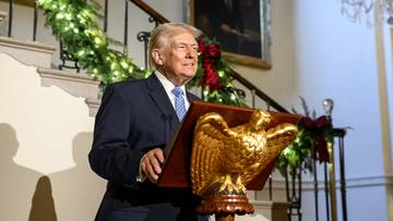 Donald Trump przemawia przy mównicy ozdobionej złotym orłem i świątecznymi dekoracjami.