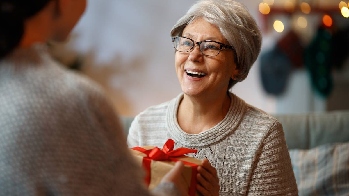 Starsza kobieta w okularach uśmiecha się, otrzymując prezent od innej osoby.