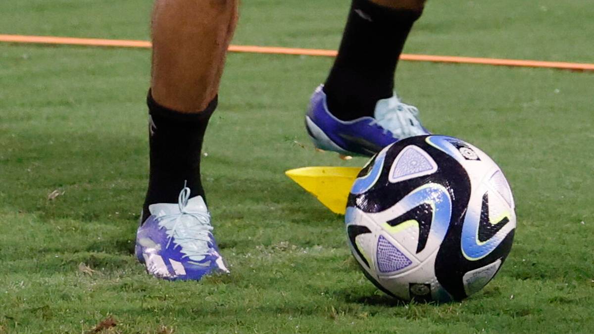 Piłkarz w butach sportowych i czarnych skarpetach kopie piłkę nożną na boisku.