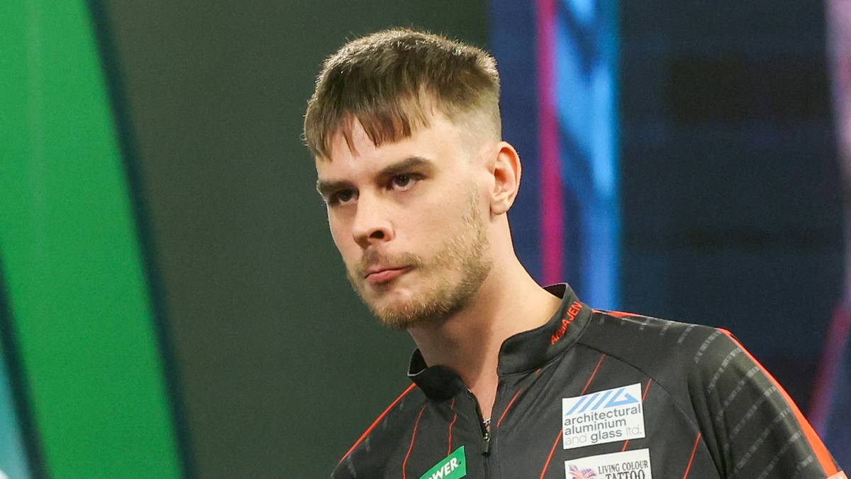 Młody mężczyzna w stroju sportowym do darta z tatuażami na ramieniu trzyma rzutkę.