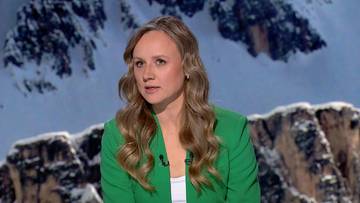 Kobieta w zielonej marynarce z mikrofonem, na tle zimowych g&oacute;r.