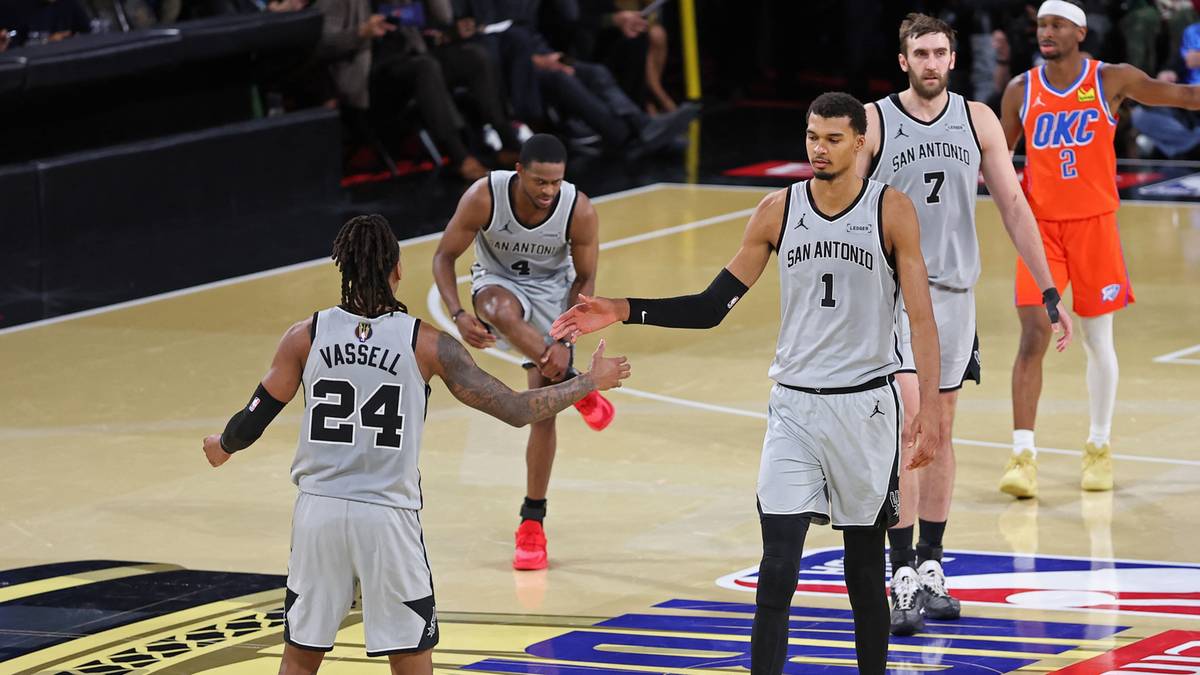 Dwóch koszykarzy w szarych strojach dotyka się dłońmi na boisku do koszykówki.