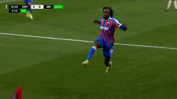 Piłkarz w czerwono-niebieskim stroju wykonuje skok na boisku piłkarskim.