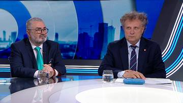 Dw&oacute;ch polityk&oacute;w, jeden w okularach i zielonym krawacie, drugi w pasiastym krawacie, siedzi przy stole w studio telewizyjnym.