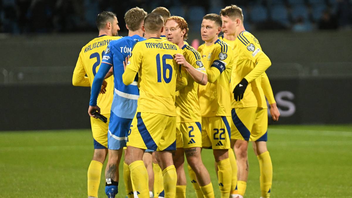 Grupa piłkarzy w żółtych strojach tworzy krąg na boisku, rozmawiając ze sobą.