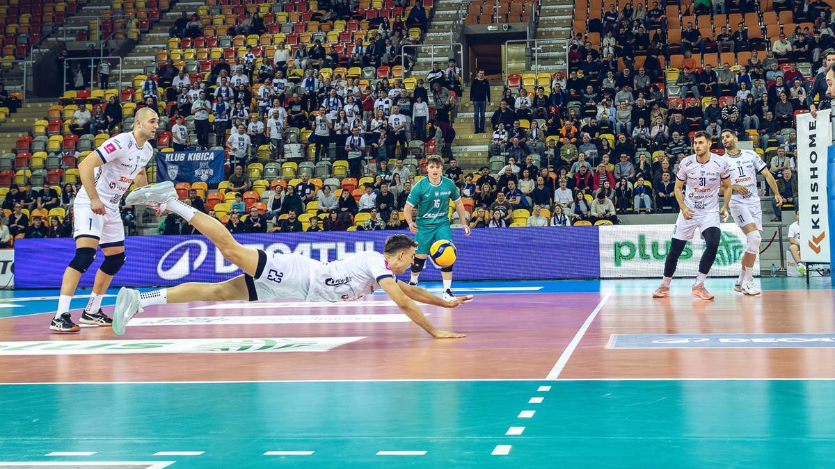 Siatkarze w akcji na parkiecie podczas meczu, jeden z zawodnik&oacute;w wykonuje wślizg po piłkę.