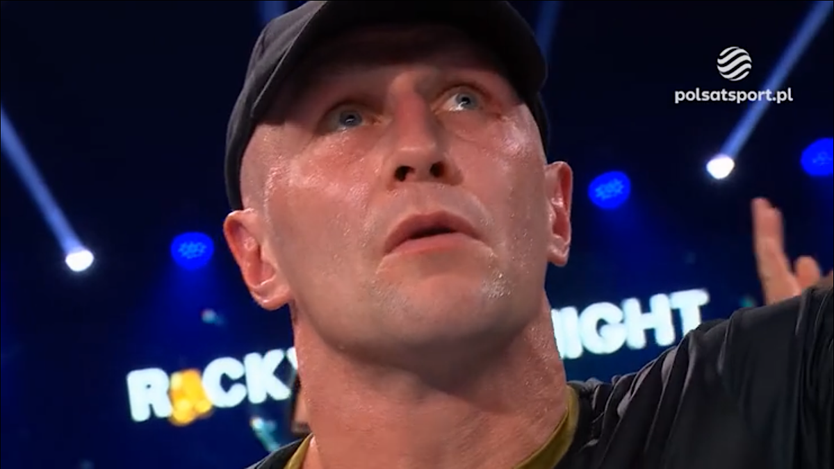 Portret mężczyzny w czapce z daszkiem i czarnym t-shircie, z widocznym potem na twarzy, patrzącego w górę.