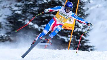 Narciarz alpejski w kombinezonie z francuską flagą ściga się na śniegu, pochylony do przodu z nartami ustawionymi r&oacute;wnolegle i kijkami narciarskimi po bokach.
