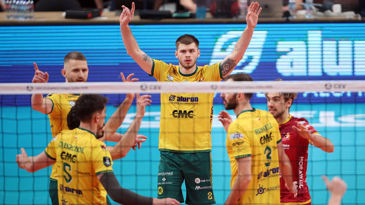 Siatkarze Aluron CMC Warty Zawiercie podczas meczu Ligi Mistrz&oacute;w, jeden z zawodnik&oacute;w unosi ręce w geście triumfu.