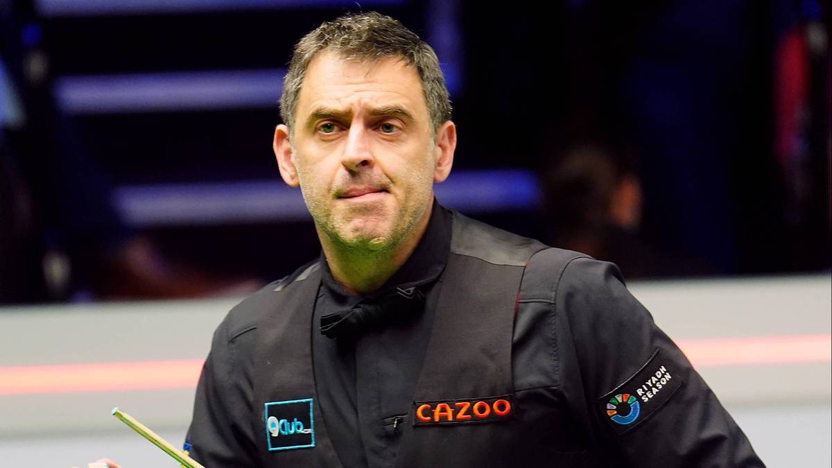 Ronnie O'Sullivan, gracz snookera, w czarnej koszuli z kamizelką i muszką, koncentruje się podczas meczu.