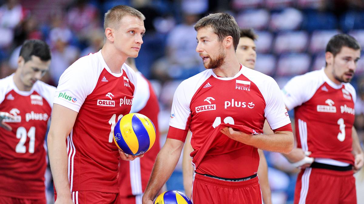 Dw&oacute;ch polskich siatkarzy w czerwonych koszulkach z białymi elementami i logo PlusLiga, patrzących na siebie podczas meczu. Jeden z nich trzyma piłkę do siatk&oacute;wki.