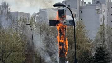 Drewniany krzyż, obity blachą, płonie z widocznym dymem i płomieniami.