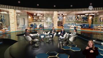 Pięciu mężczyzn siedzi w okrągłym studiu telewizyjnym, otoczeni przeszklonymi ścianami, za którymi widać wystrój kawiarniany. W rogu ekranu po prawej stronie znajduje się kobieta gestykulująca w kierunku kamery.