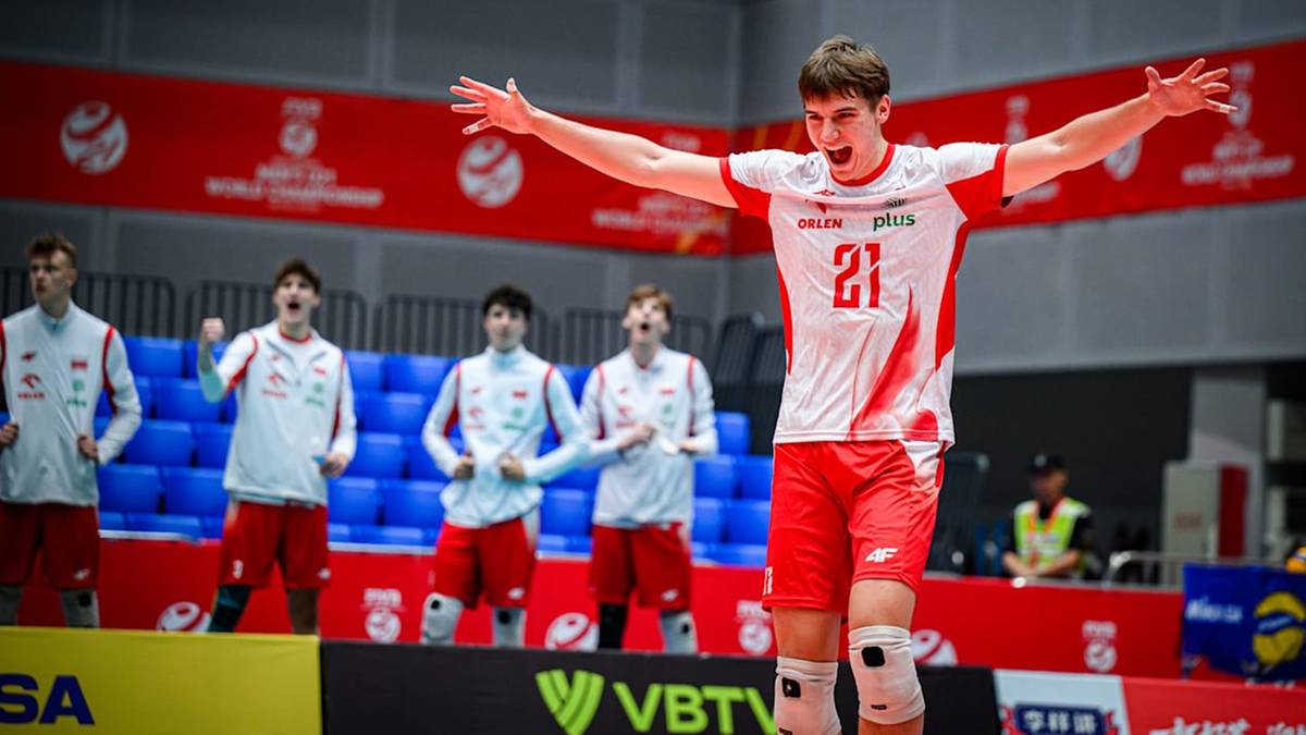 Młody mężczyzna w stroju siatkarskim świętuje zwycięstwo z rękami uniesionymi do góry, na tle innych zawodników i trybun.