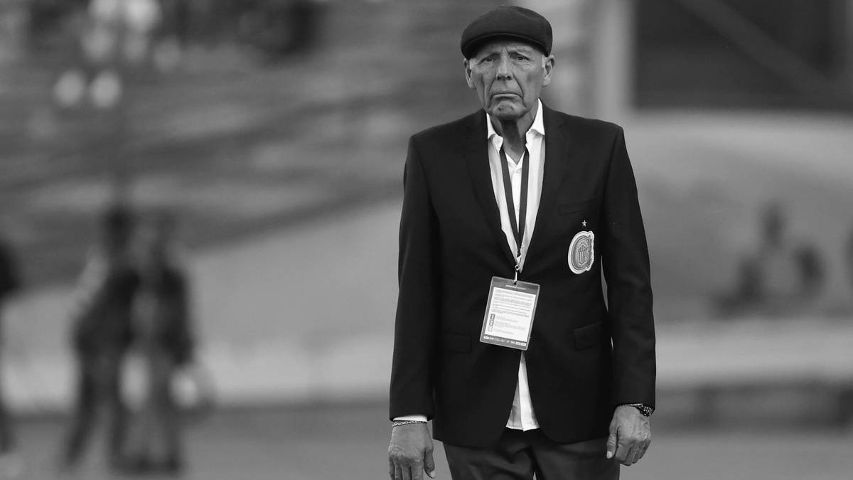 Czarno-białe zdjęcie przedstawiające starszego mężczyznę w czapce i garniturze, patrzącego przed siebie z poważną miną.