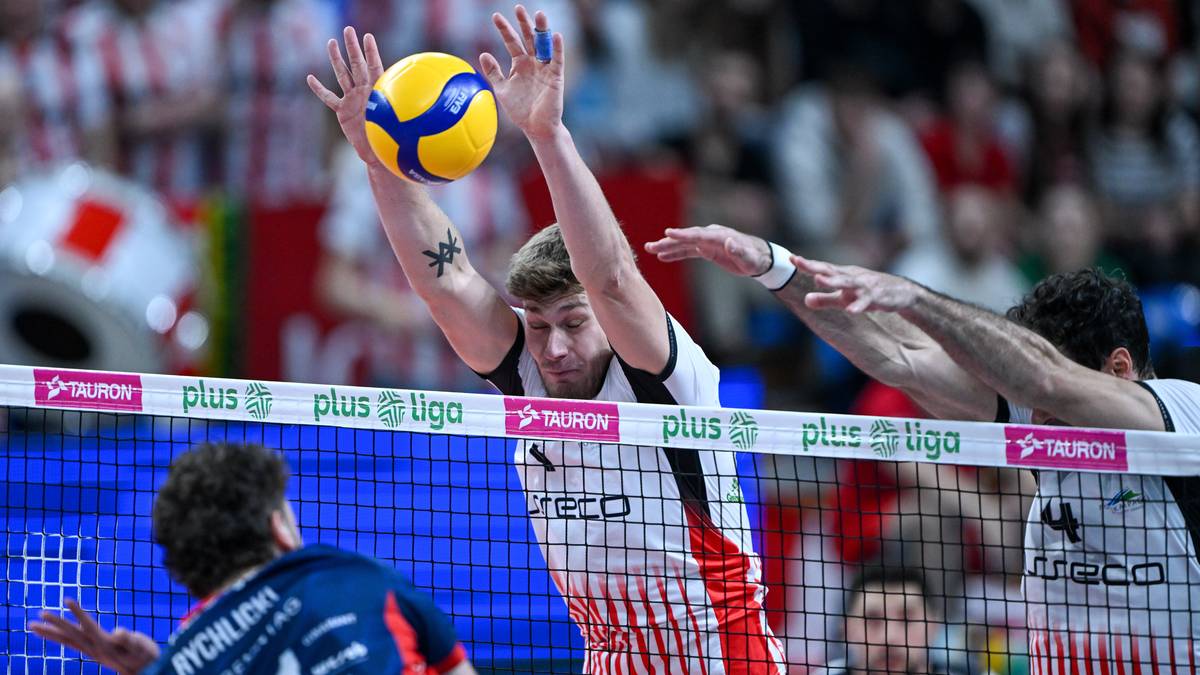 Siatkarz w białej koszulce zagrywa piłkę, a zawodnik w granatowej próbuje ją zablokować.