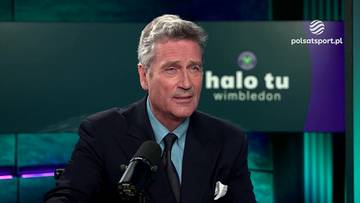 Mężczyzna w garniturze siedzi przed mikrofonem w studio telewizyjnym z napisem "halo tu wimbledon" w tle.
