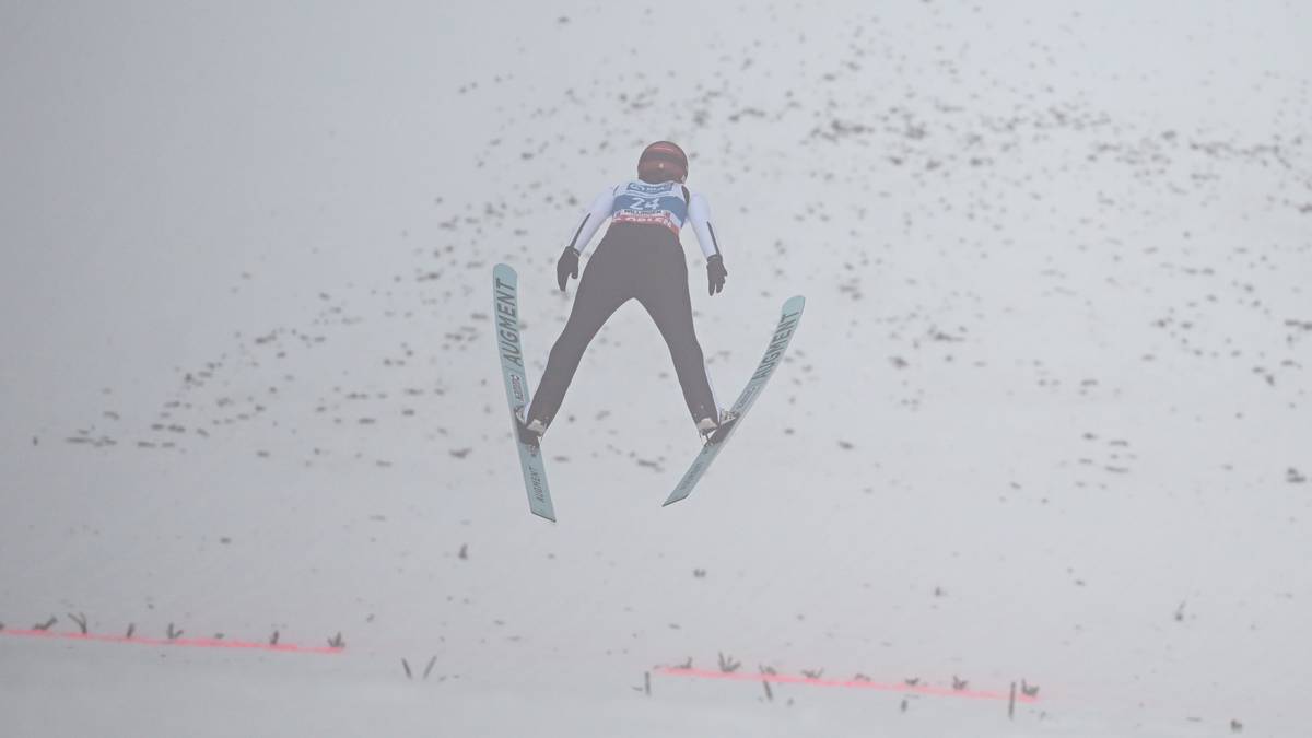 Skoczkini narciarska w locie na tle mglistego krajobrazu.