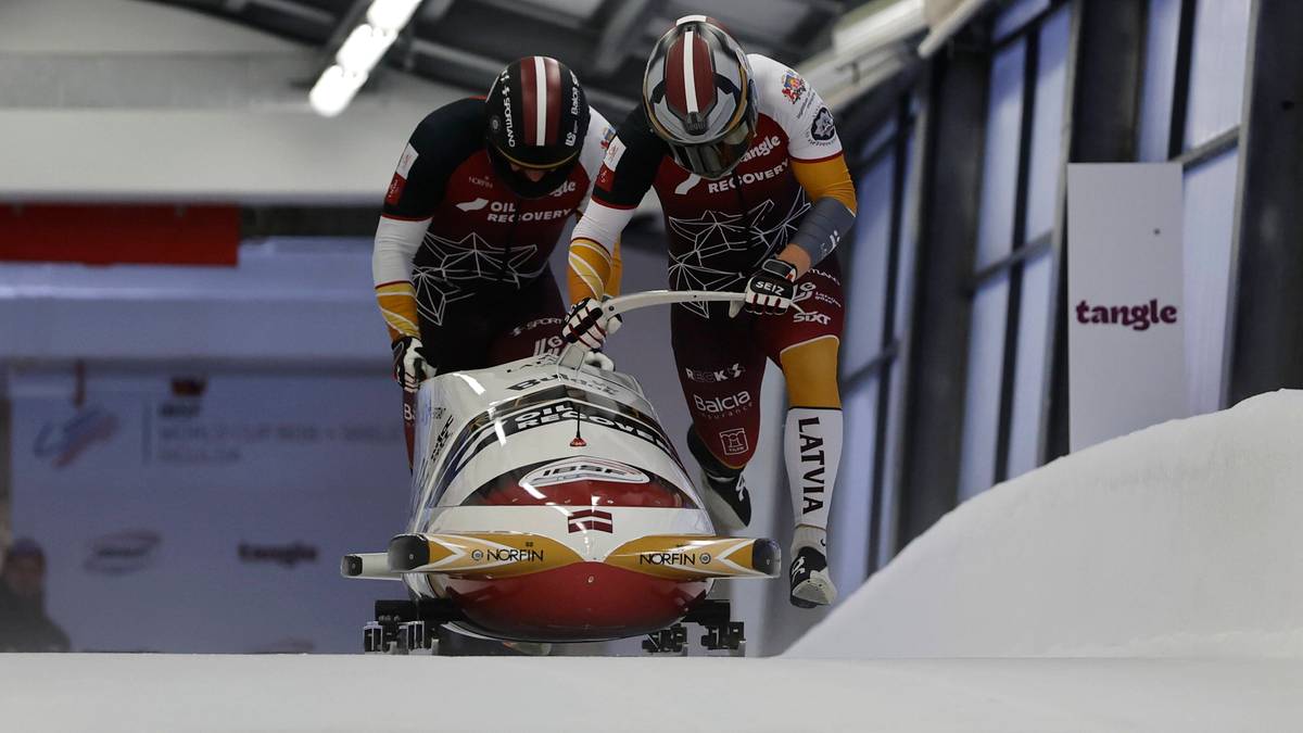 Dw&oacute;ch zawodnik&oacute;w w kaskach przygotowuje się do startu w bobslejach.