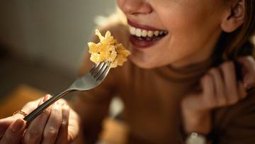 Uśmiechnięta kobieta jedząca widelec z makaronem.