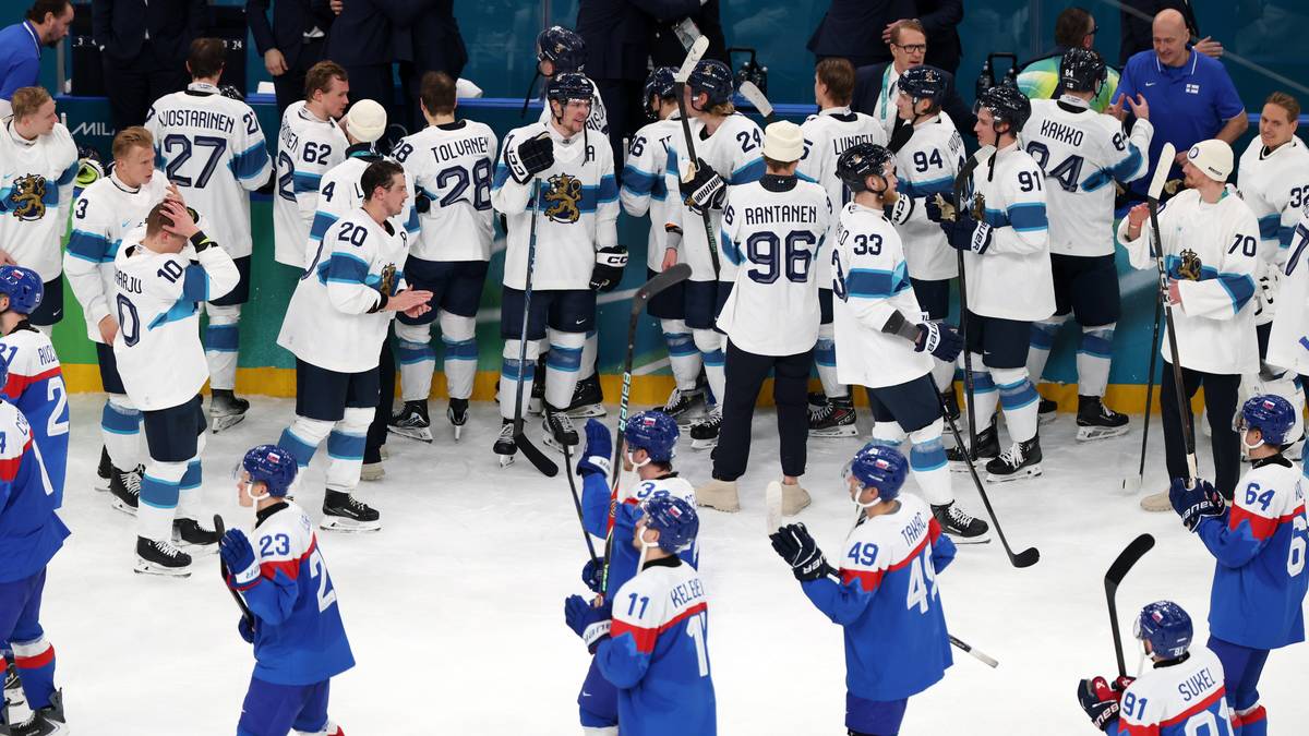 Drużyna hokejowa w niebieskich strojach świętuje na lodowisku po meczu, na drugim planie stoją gracze w białych i niebieskich strojach.