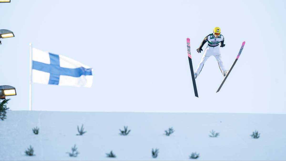 Skoczek narciarski w powietrzu z polską flagą w tle.